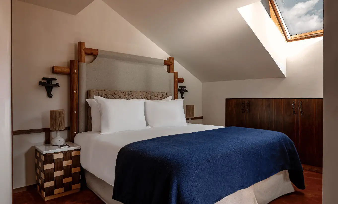Bedroom with a blue bedspread, wooden headboard and sloped ceiling in the Suite Solaise at Experimental Chalet Val d'Isère