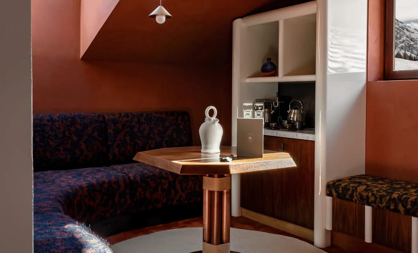 Cosy corner with terracotta walls, a dark blue velvet sofa and a wooden side table in the Solaise Suite at Experimental Chalet Val d'Isère