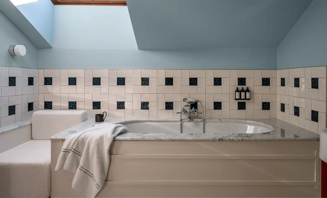 Blue-toned bathroom with a freestanding bathtub, geometric tiled walls and a skylight in the Iseran Suite at Experimental Chalet Val d'Isère