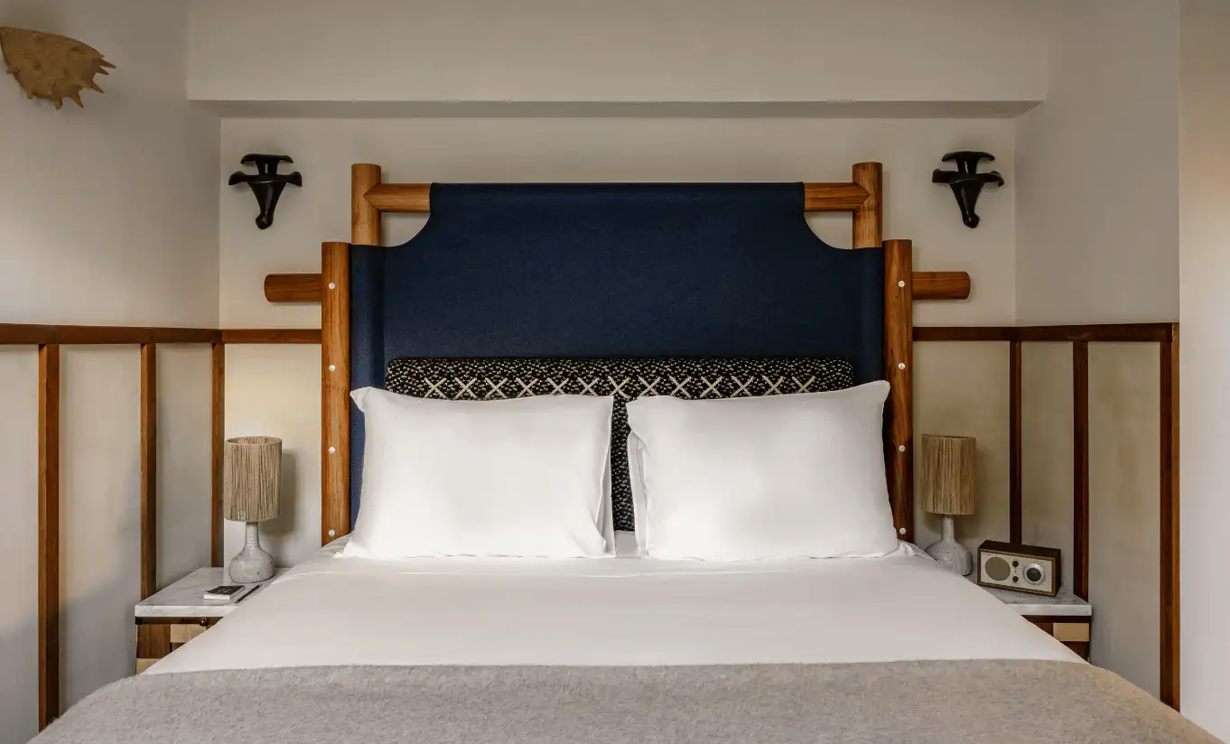 Bedroom with a white double bed, navy blue headboard and wooden posts in the Iseran Suite at Experimental Chalet Val d'Isère