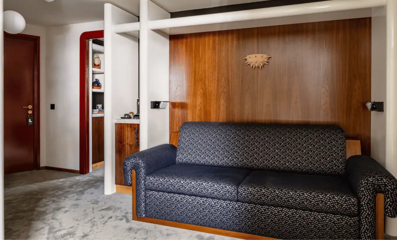 Living area with a dark blue sofa and warm wooden wall panelling in the Glacier Suite with Balcony at Experimental Chalet Val d'Isère