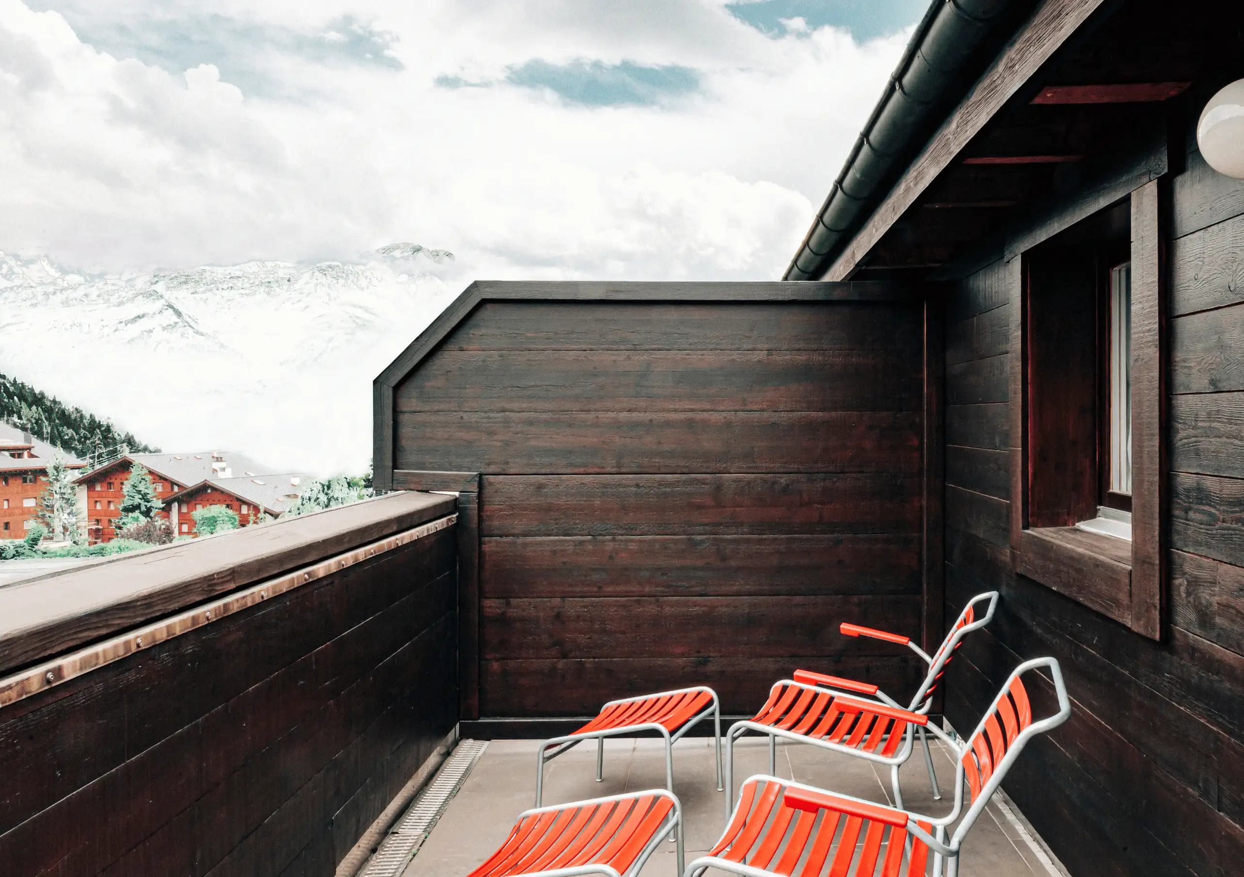 Private terrace with red chairs and a view of the alpine village in the Junior Suite Terrace at Experimental Chalet Verbier