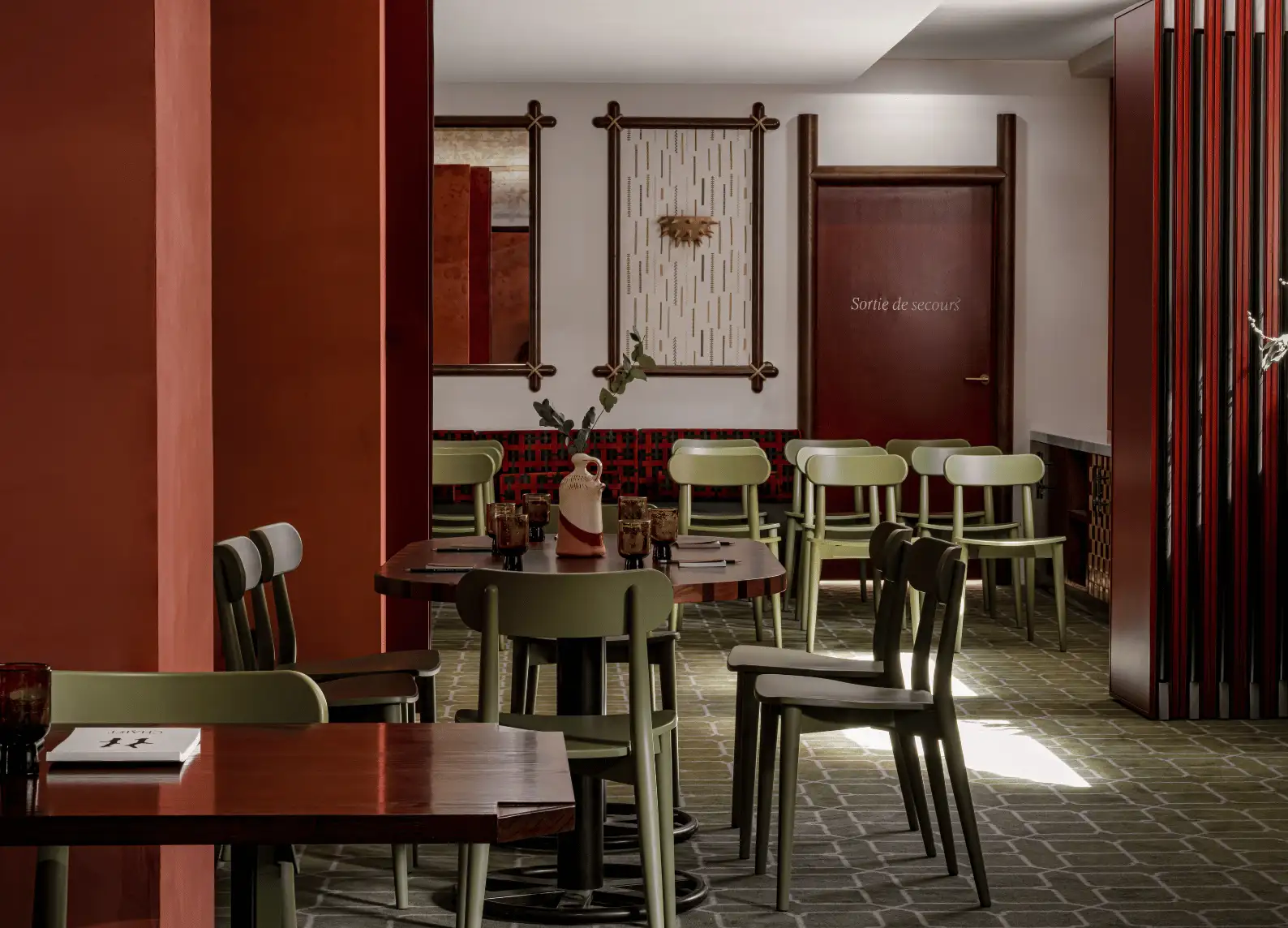 A dining room with warm tones, characterized by red walls, wooden chairs, and framed wall decorations.