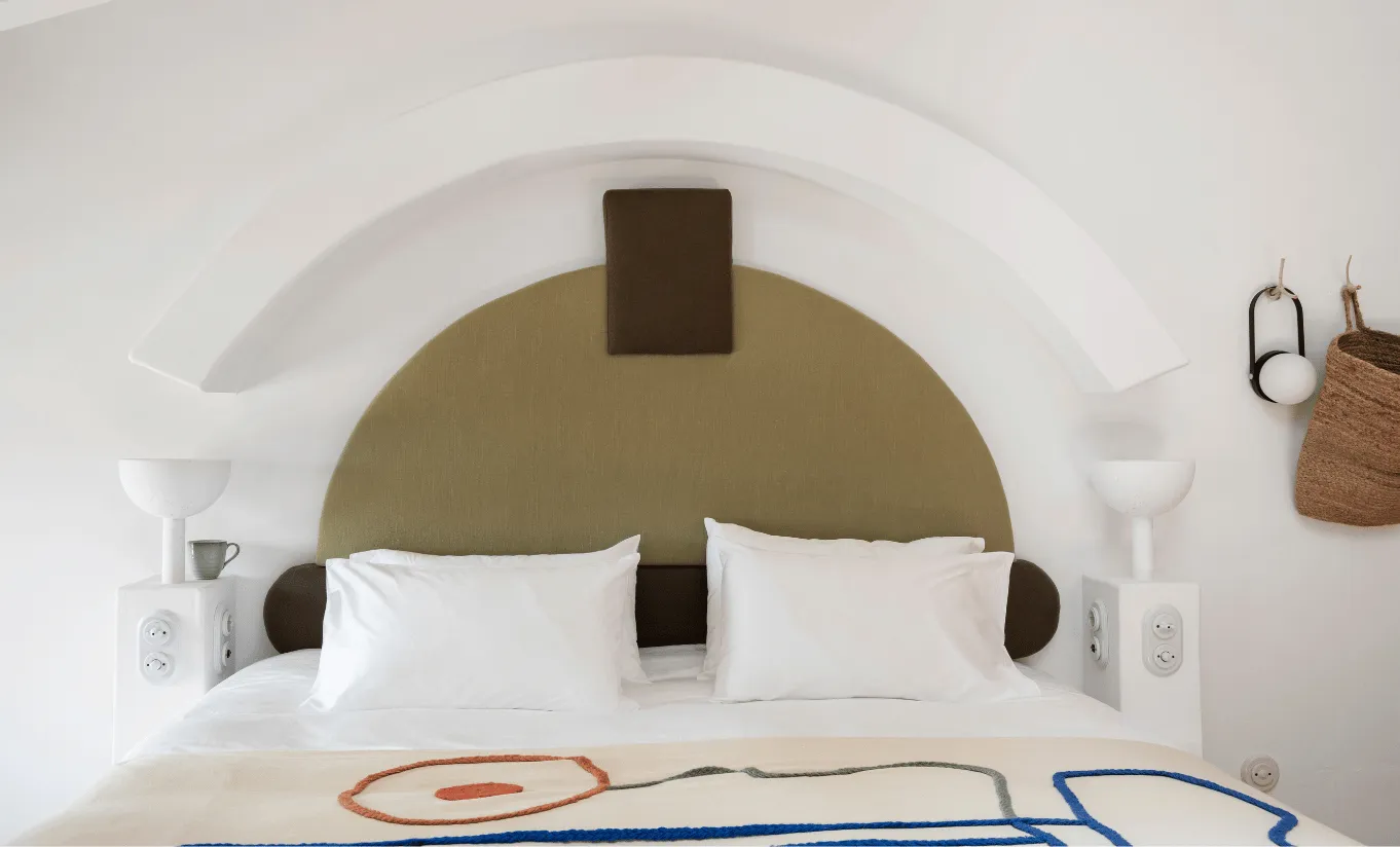 Whitewashed bedroom with a sculptural ochre and olive arched alcove, white linen bedding and minimalist decor at Menorca Experimental hotel, Experimental Group.