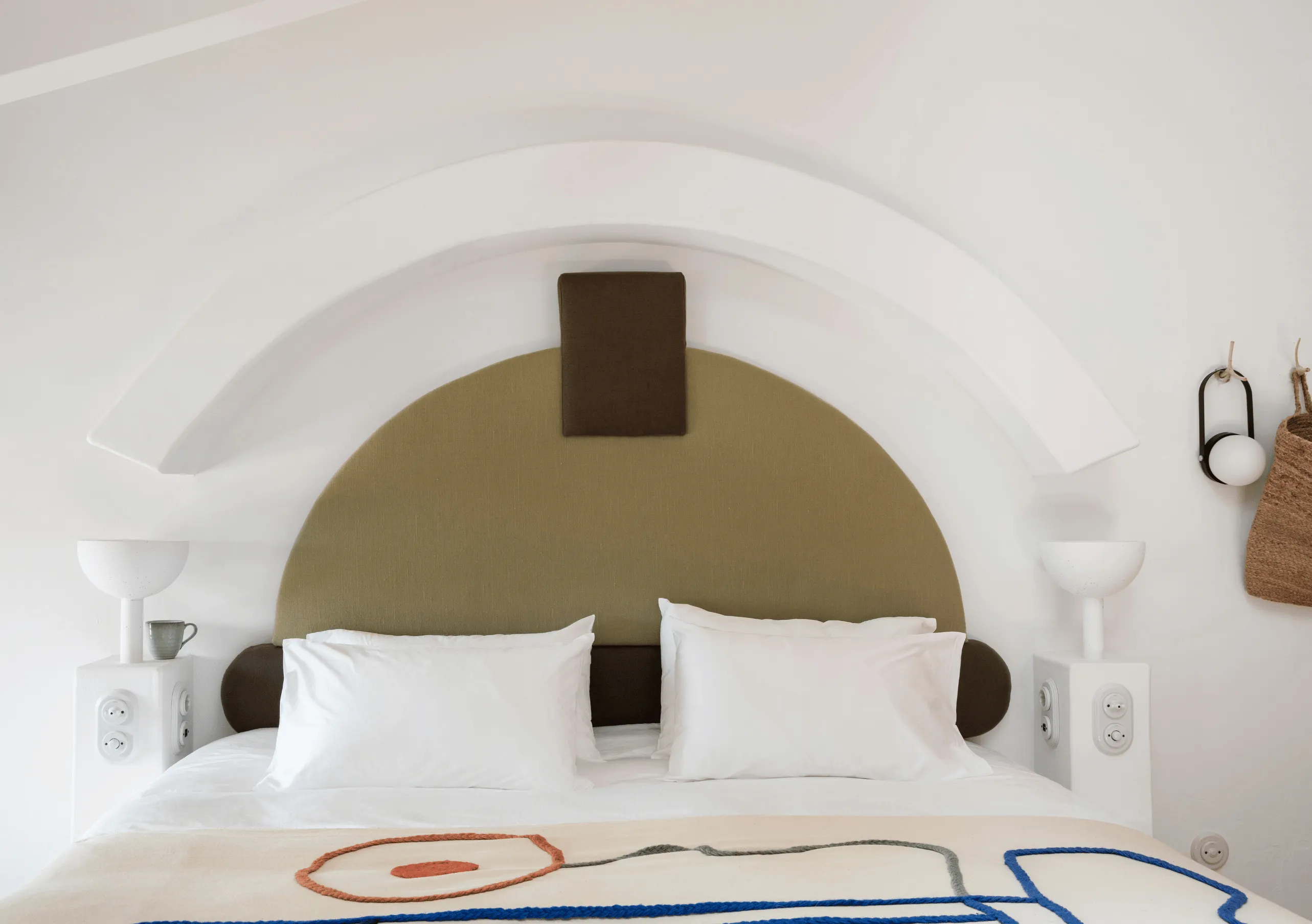 Bright whitewashed bedroom with a bold ochre semicircular arch headboard, white linen bedding and graphic floor detail at Menorca Experimental hotel, Experimental Group.