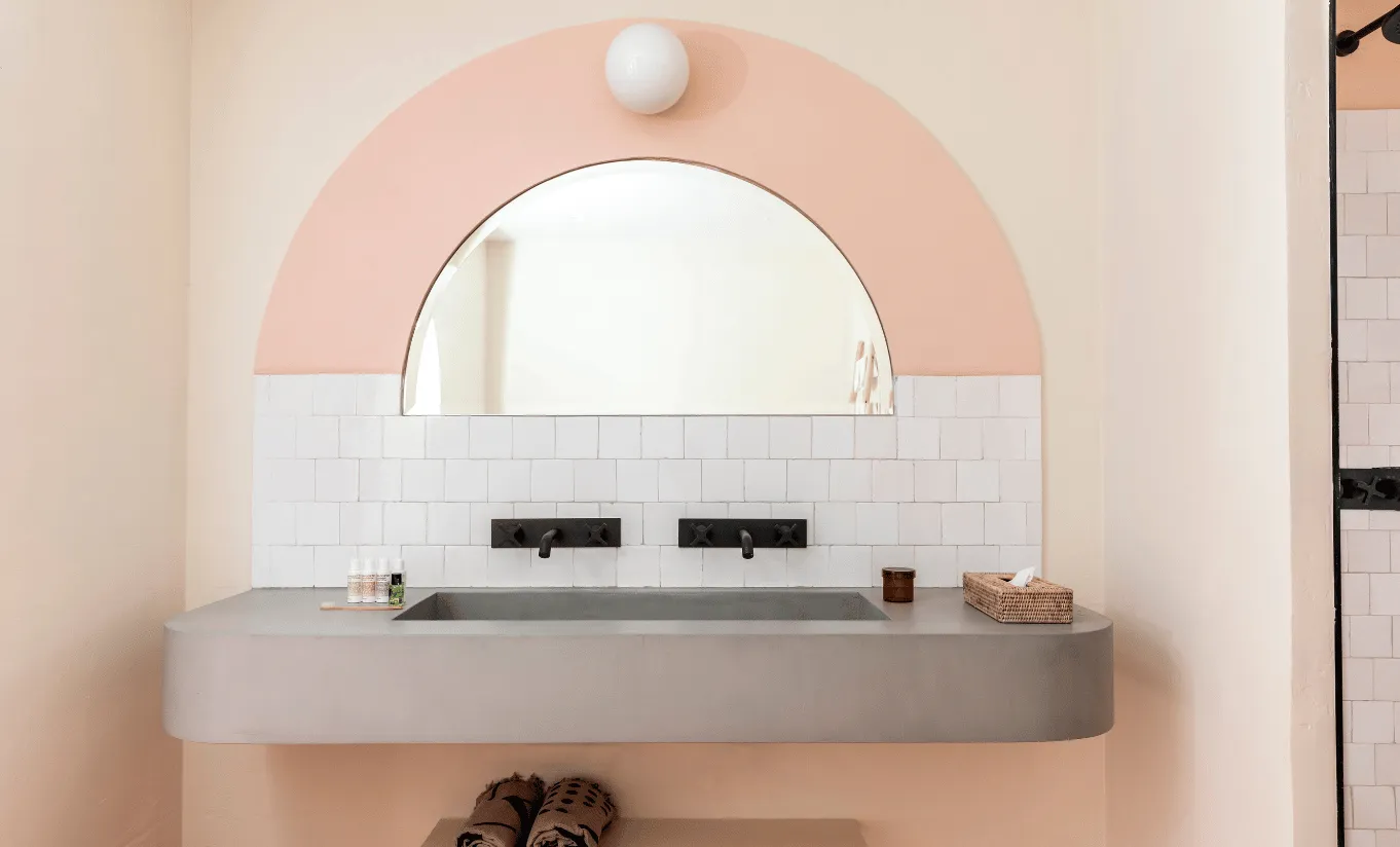 Sleek bathroom vanity with a floating concrete basin, matte black faucet and soft pink semicircular mirror at Menorca Experimental hotel, Experimental Group.
