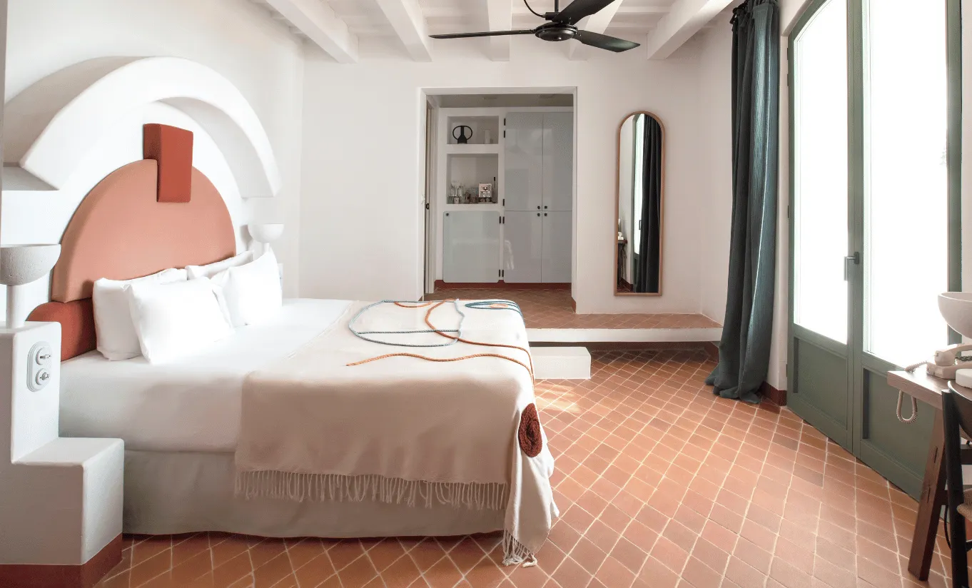 Airy and spacious bedroom with terracotta arched headboard, light wood flooring and ceiling fan at Menorca Experimental hotel, Experimental Group.