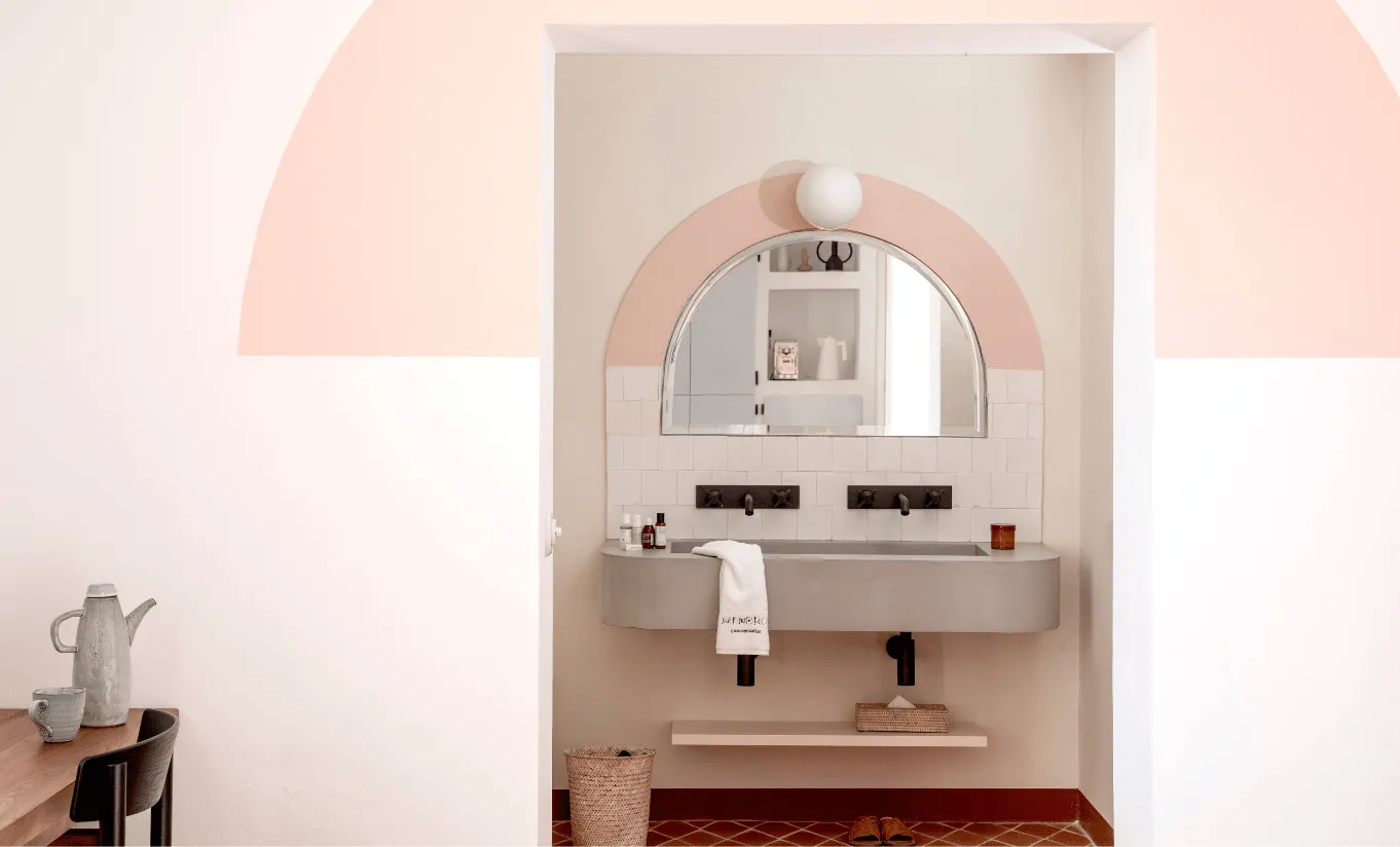 Elegant bathroom with dual vessel sinks, a round mirror and soft pink arched alcove at Menorca Experimental hotel, Experimental Group.