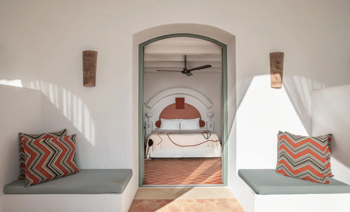Inviting bedroom entrance with a stone arched doorway, terracotta floor tiles and woven cushions at Menorca Experimental hotel, Experimental Group.