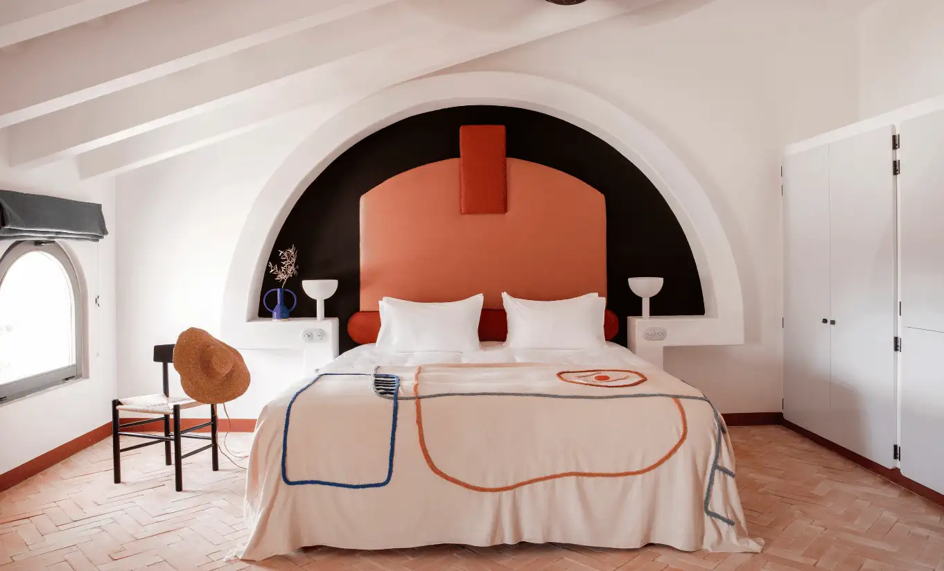Sculptural bedroom with dramatic black and terracotta arched alcove, upholstered headboard and woven leather chair at Menorca Experimental hotel, Experimental Group.