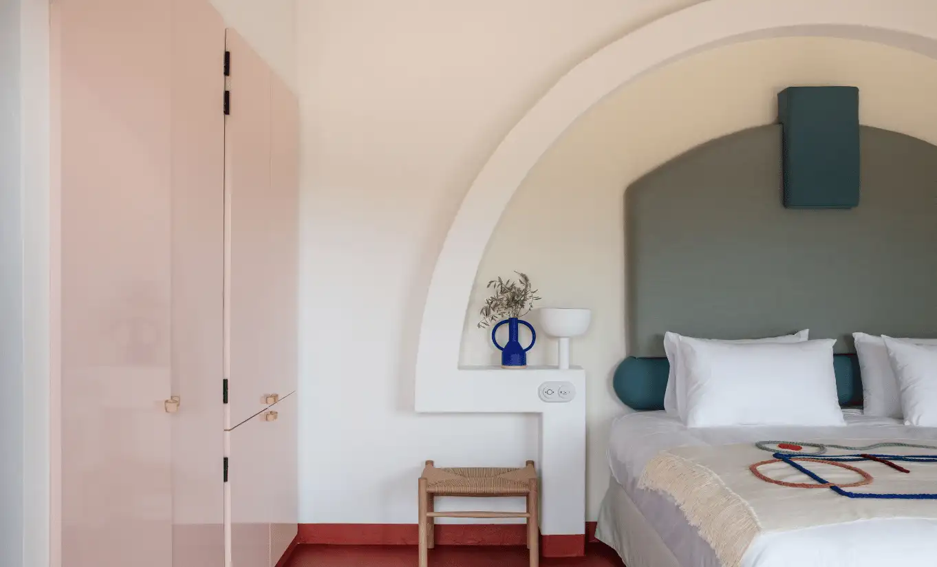Intimate bedroom with sage green arched niche, grey upholstered headboard and wooden stool at Menorca Experimental hotel, Experimental Group.