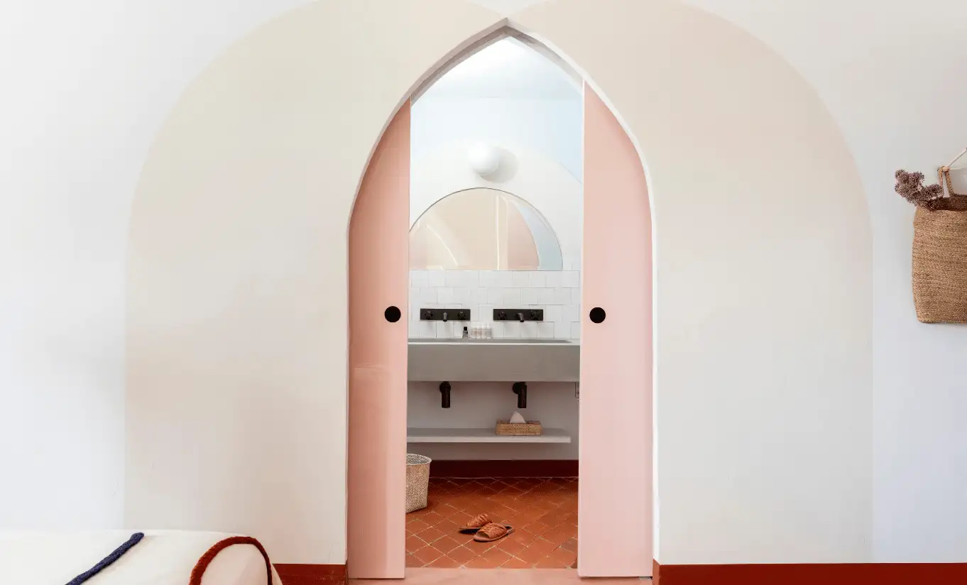 Whitewashed corridor with a delicate pointed arch doorway leading to a softly lit bedroom at Menorca Experimental hotel, Experimental Group.