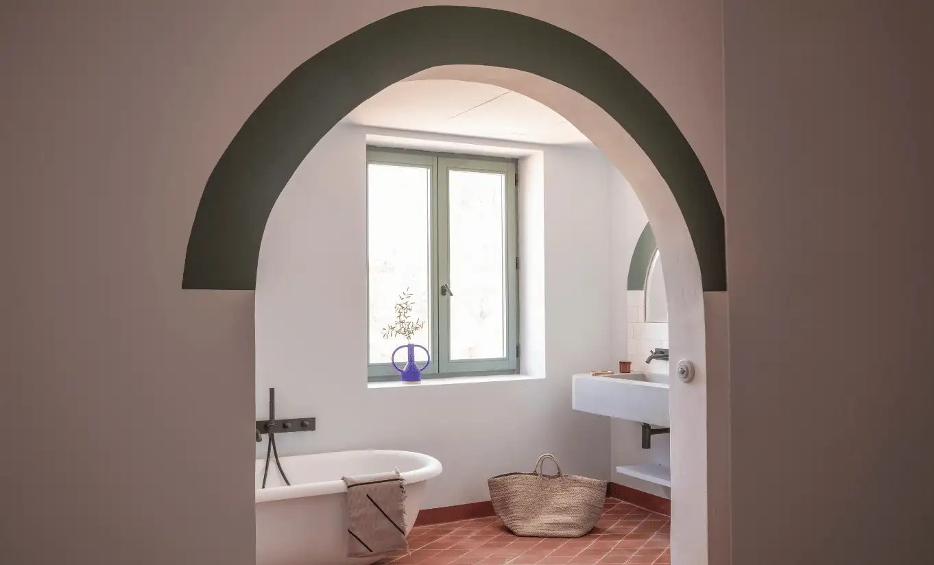 Arched doorway revealing a bright bathroom with freestanding bathtub and terracotta floor tiles at Menorca Experimental hotel, Experimental Group.