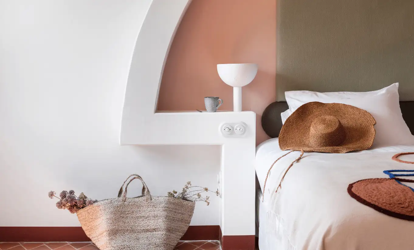 Guest relaxing in a sunlit bedroom with terracotta arched alcove, white bedding and bedside lamp at Menorca Experimental hotel, Experimental Group.