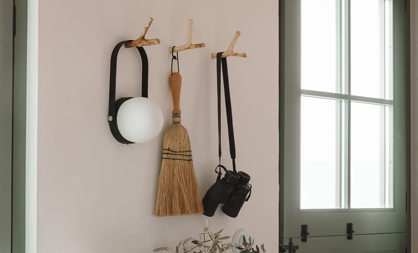 Rustic entryway with wall-mounted wooden hooks, artisan broom and brushes in a whitewashed corridor at Menorca Experimental hotel, Experimental Group.