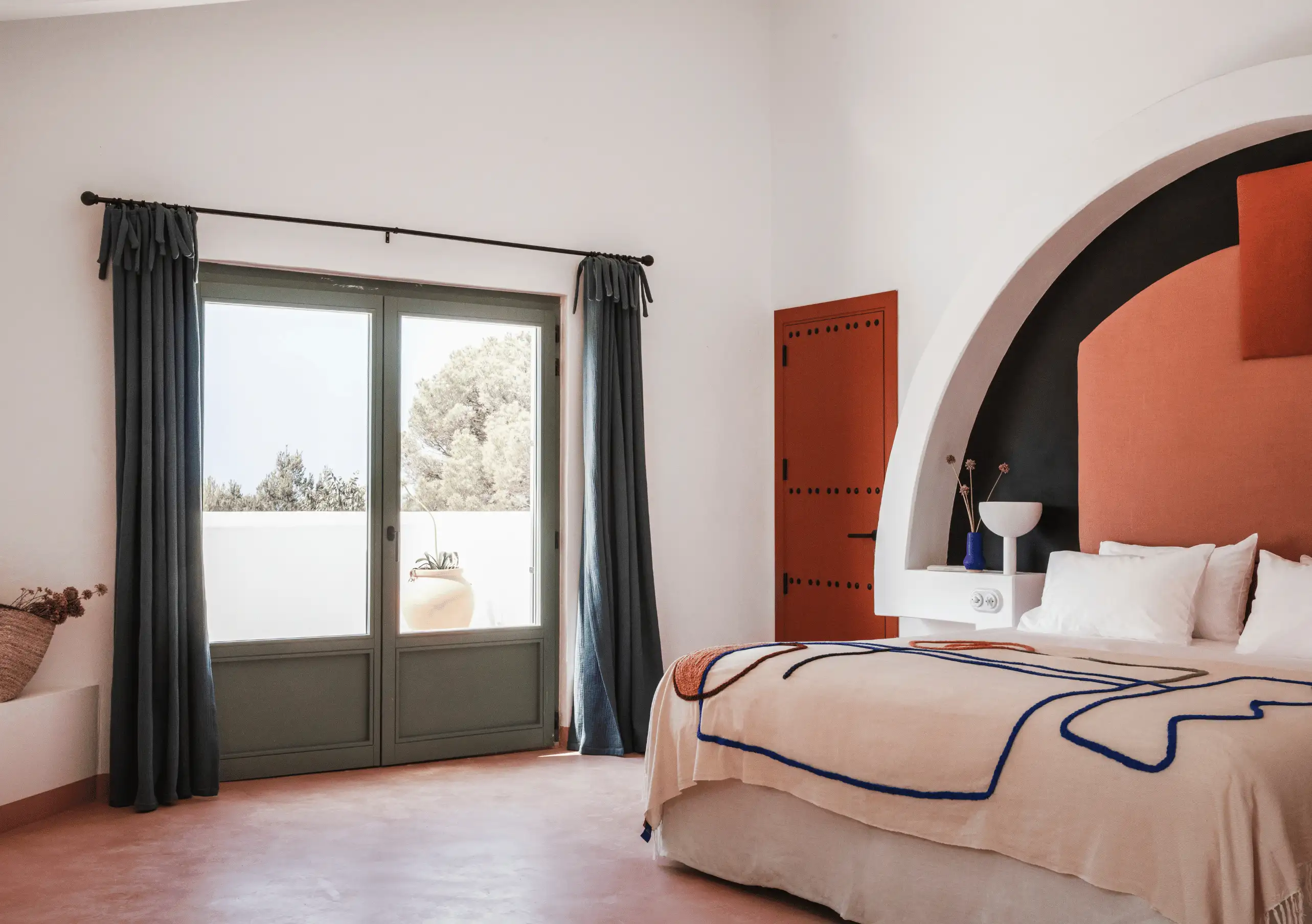 Sun-filled bedroom with rustic terracotta arch, dark curtains and views of the outdoor terrace – Menorca Experimental hotel, Experimental Group.
