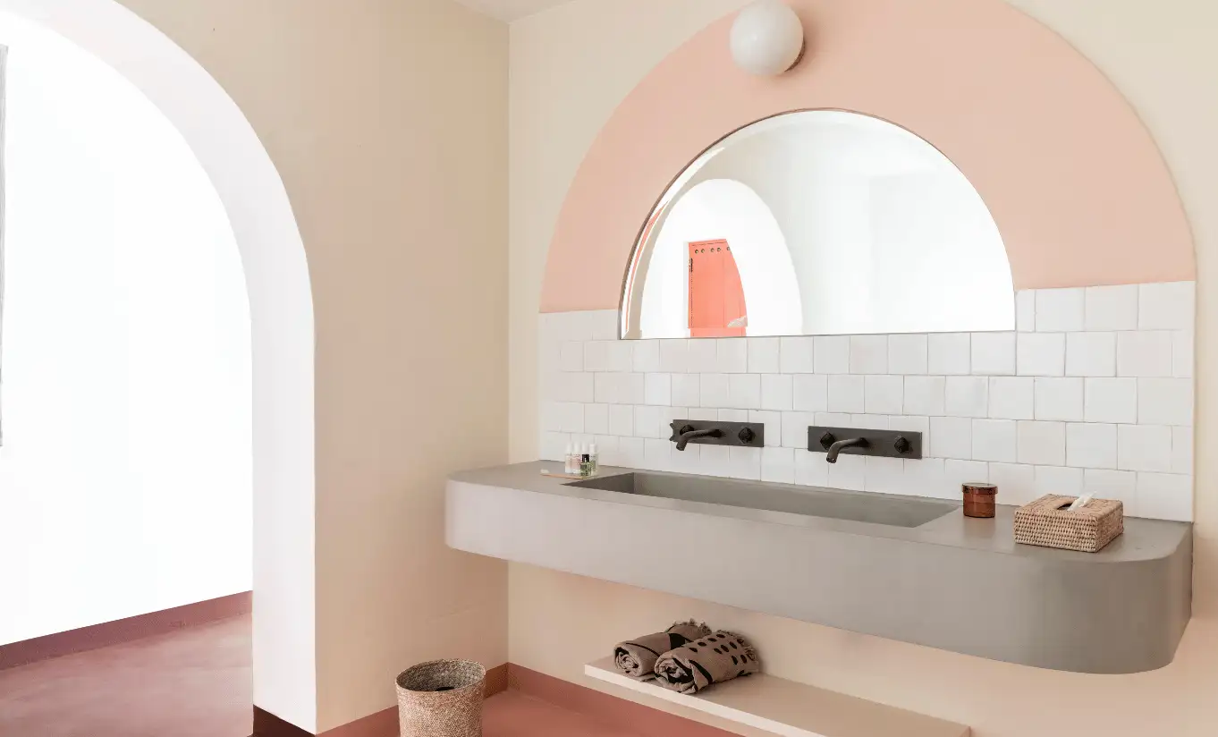 Concrete double sink vanity under a pink arched mirror in a soft pastel bathroom – Menorca Experimental hotel, Experimental Group.