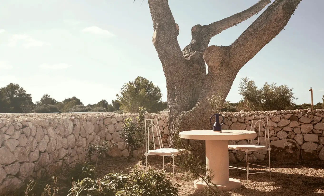 Menorca Experimental by Experimental Group – secluded stone terrace with wooden bistro table and chairs set beneath a centuries-old olive tree