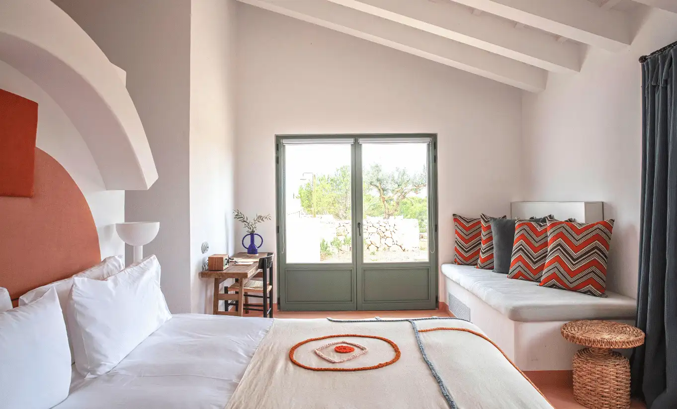 Menorca Experimental hotel bright bedroom with terracotta headboard, white bedding and garden view through large windows