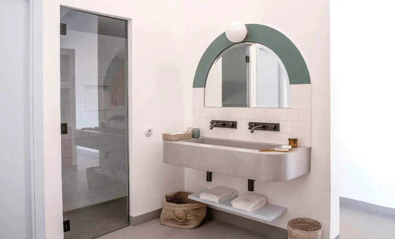 Menorca Experimental Group minimalist bathroom with sage green arched mirror, concrete double sink and natural light