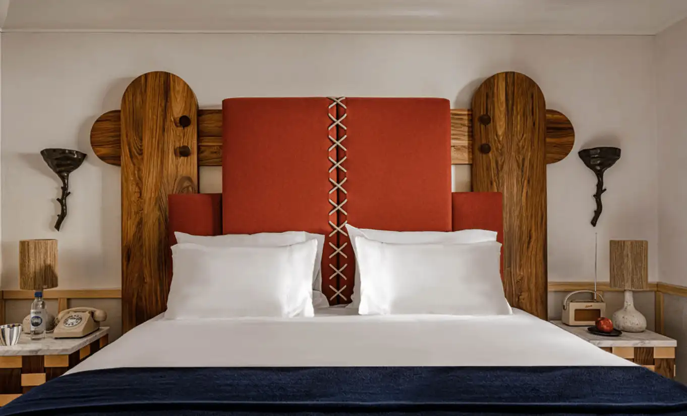 Refined alpine bedroom with a bold terracotta and geometric wood-panelled headboard, white linen bedding and warm ambient lighting at Experimental Chalet Verbier, Experimental Group.