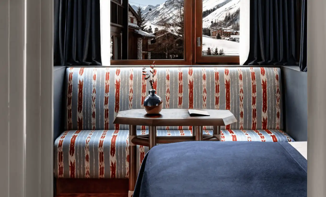 Cozy window nook with a printed upholstered banquette, scatter cushions and a snow-dusted mountain view at Experimental Chalet Verbier, Verbier, Experimental Group.