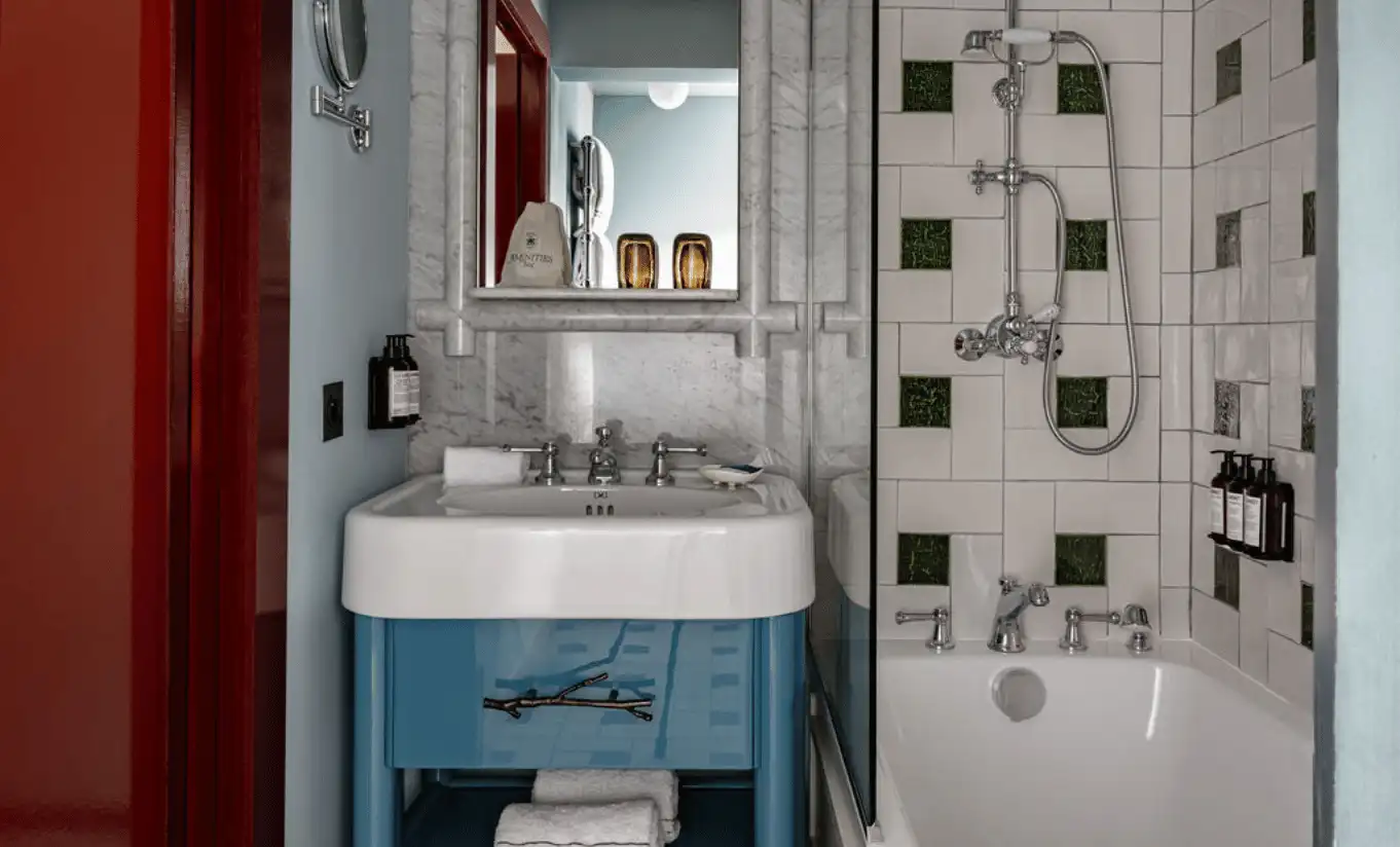 Compact bathroom with a turquoise vanity unit, white vessel sink, wall mirror and graphic patterned tile surround at Experimental Chalet Verbier, Experimental Group.