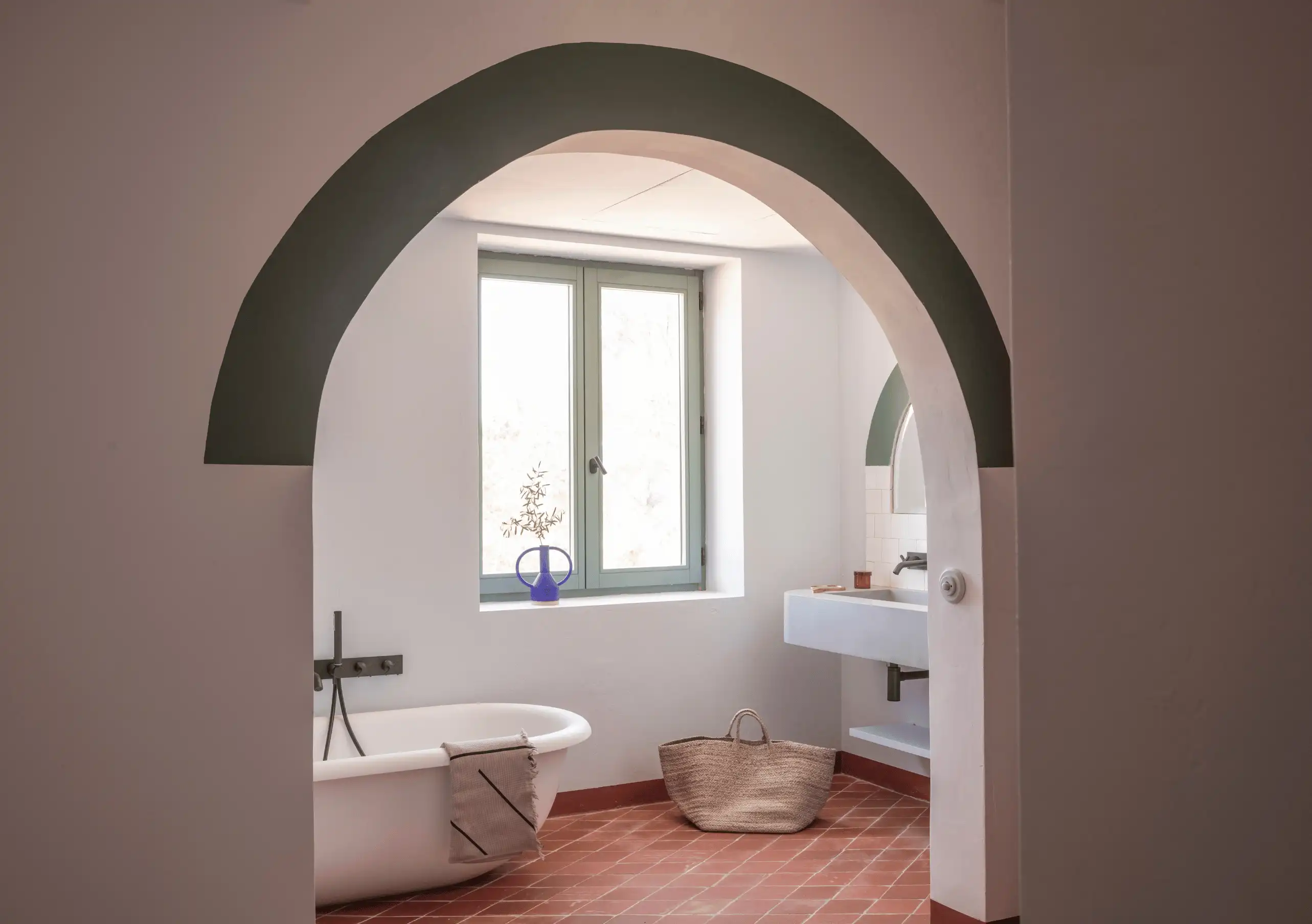 Sunlit bathroom with freestanding bathtub, wall-mounted toilet and terracotta floor framed by a wide plaster arch at Menorca Experimental hotel, Experimental Group.