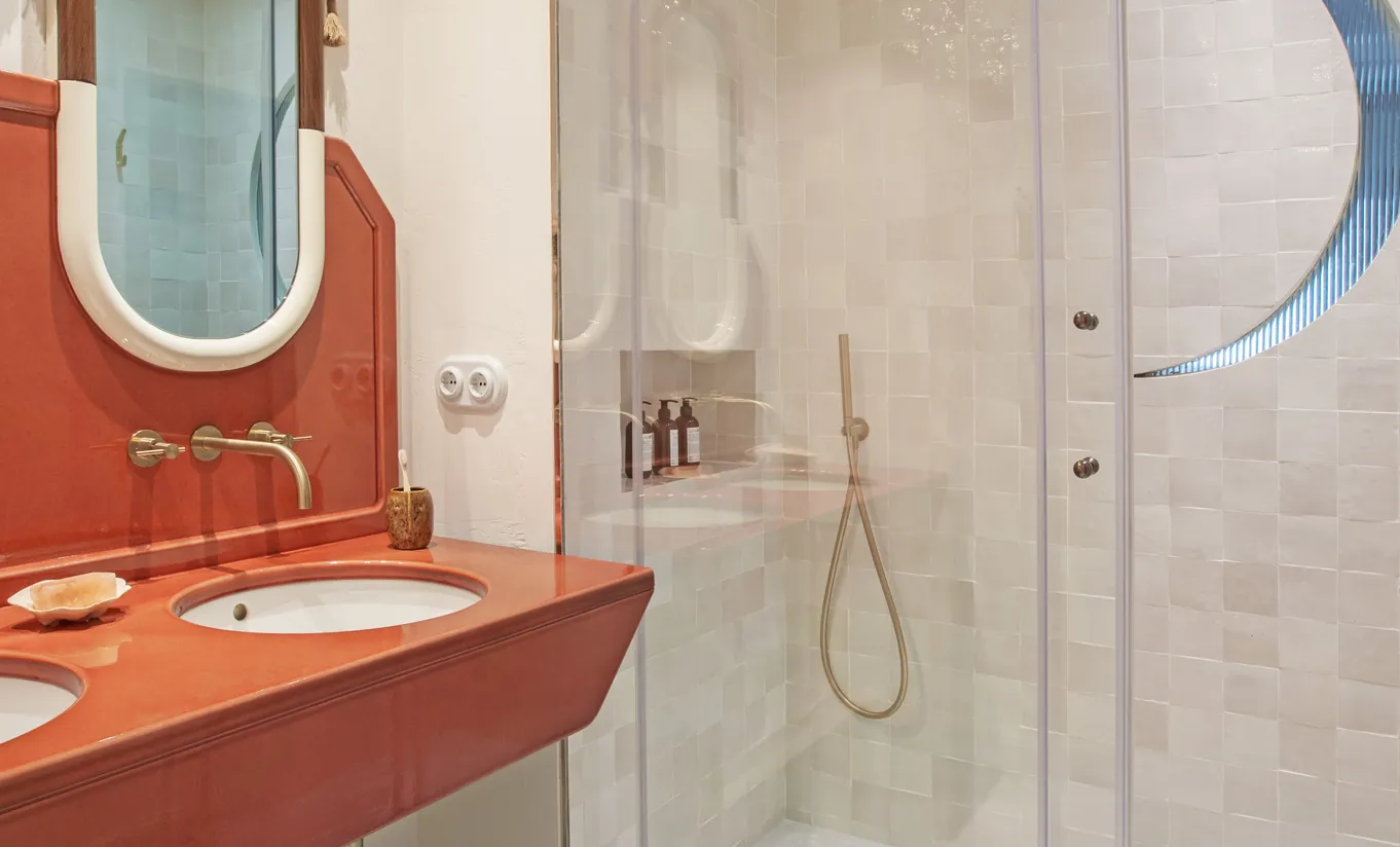 Vibrant bathroom with terracotta red vanity, oval mirror, vessel sink and glass-enclosed shower at Montesol Experimental hotel, Experimental Group.