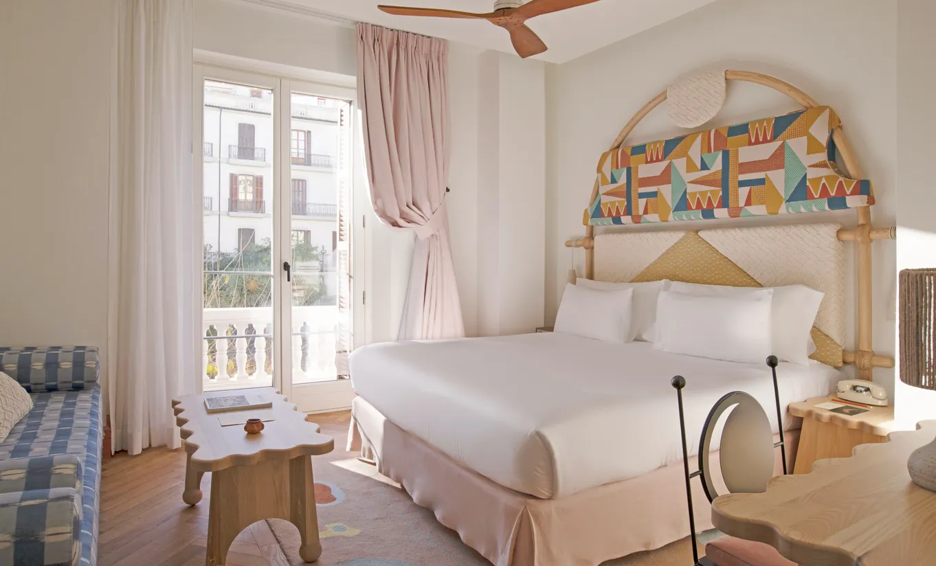 Romantic bedroom with ornate painted arch headboard, white linen bedding, rattan furniture and balcony view at Montesol Experimental hotel, Experimental Group.