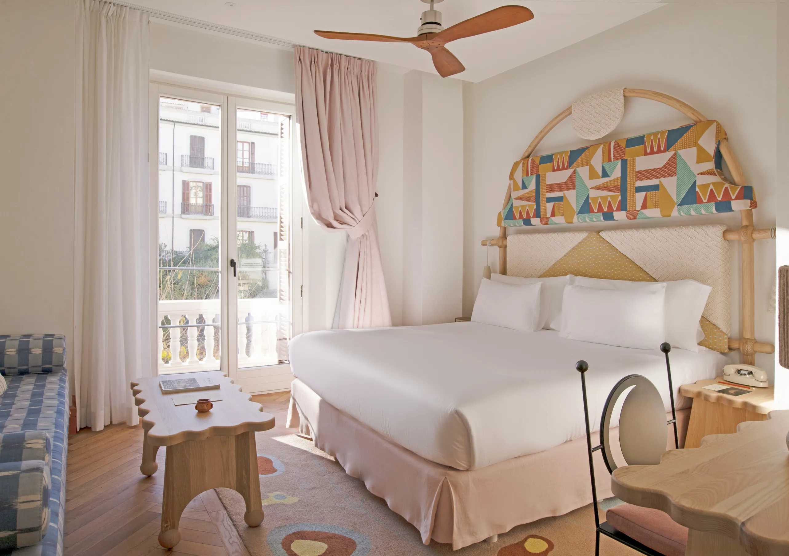 Elegant and luminous bedroom with an elaborately painted arch headboard, white linen, rattan furniture and city-view balcony at Montesol Experimental hotel, Experimental Group.