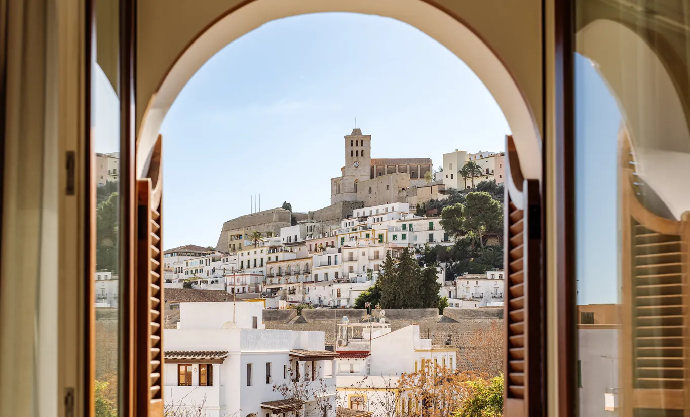 Breathtaking view of Ibiza's historic Dalt Vila fortress and old town rooftops framed by a classic arched window at Montesol Experimental hotel, Ibiza, Experimental Group.