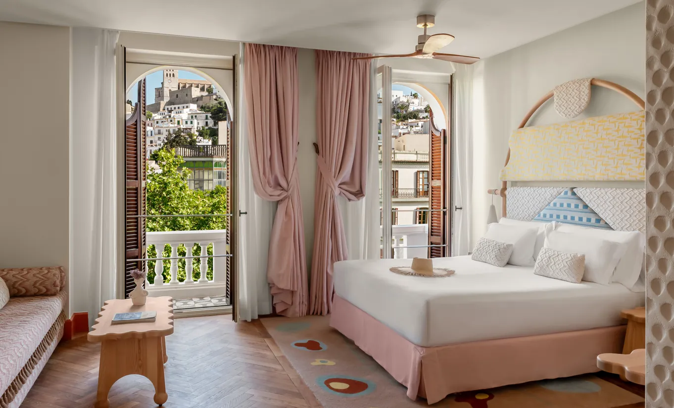 Elegant bedroom with ornate white arched headboard, blush pink drapery, lush garden balcony view and ceiling fan at Montesol Experimental hotel, Experimental Group.