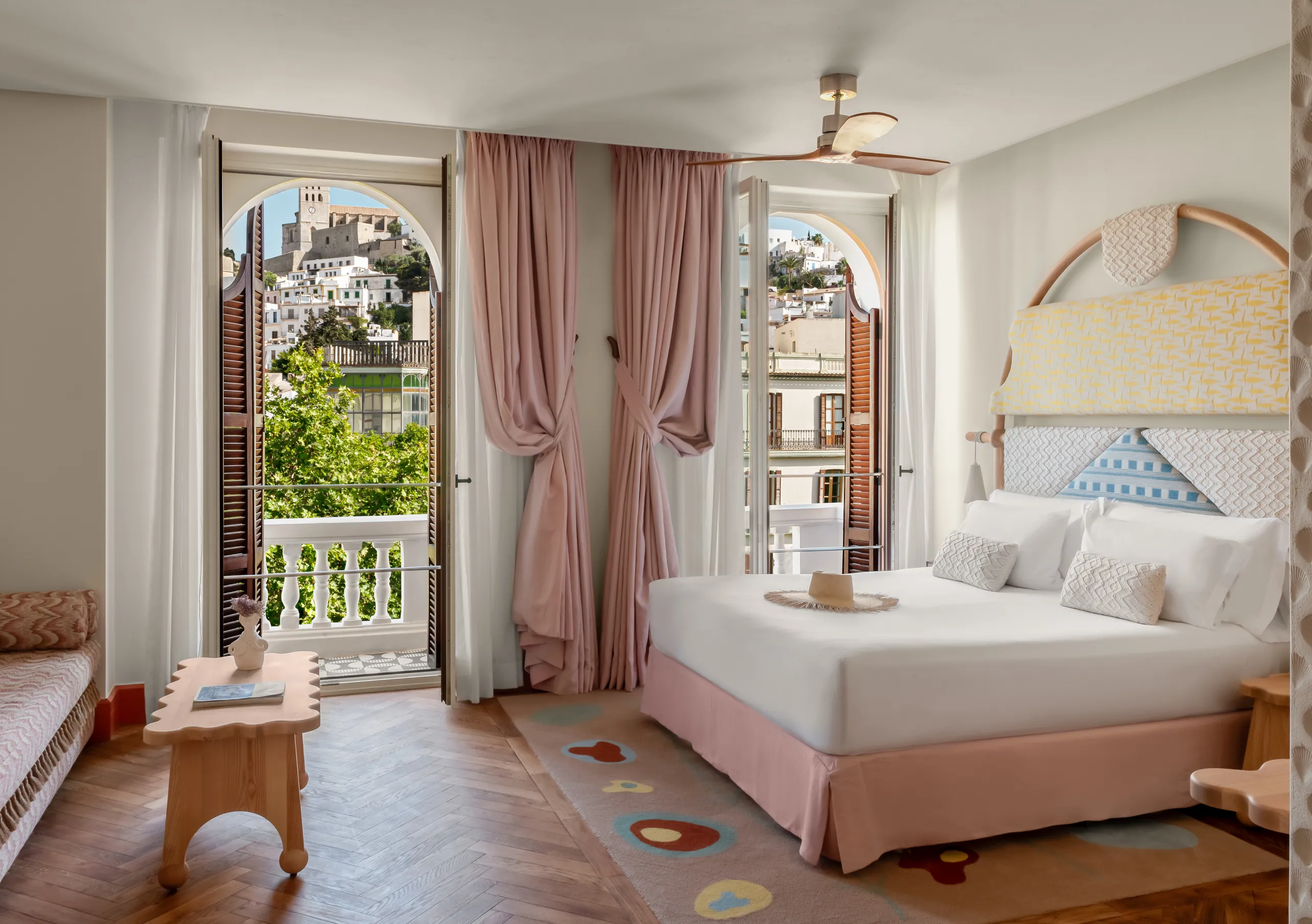 Romantic and airy bedroom with a pale blue painted headboard, soft pink curtains, rattan side table and garden balcony at Montesol Experimental hotel, Experimental Group.