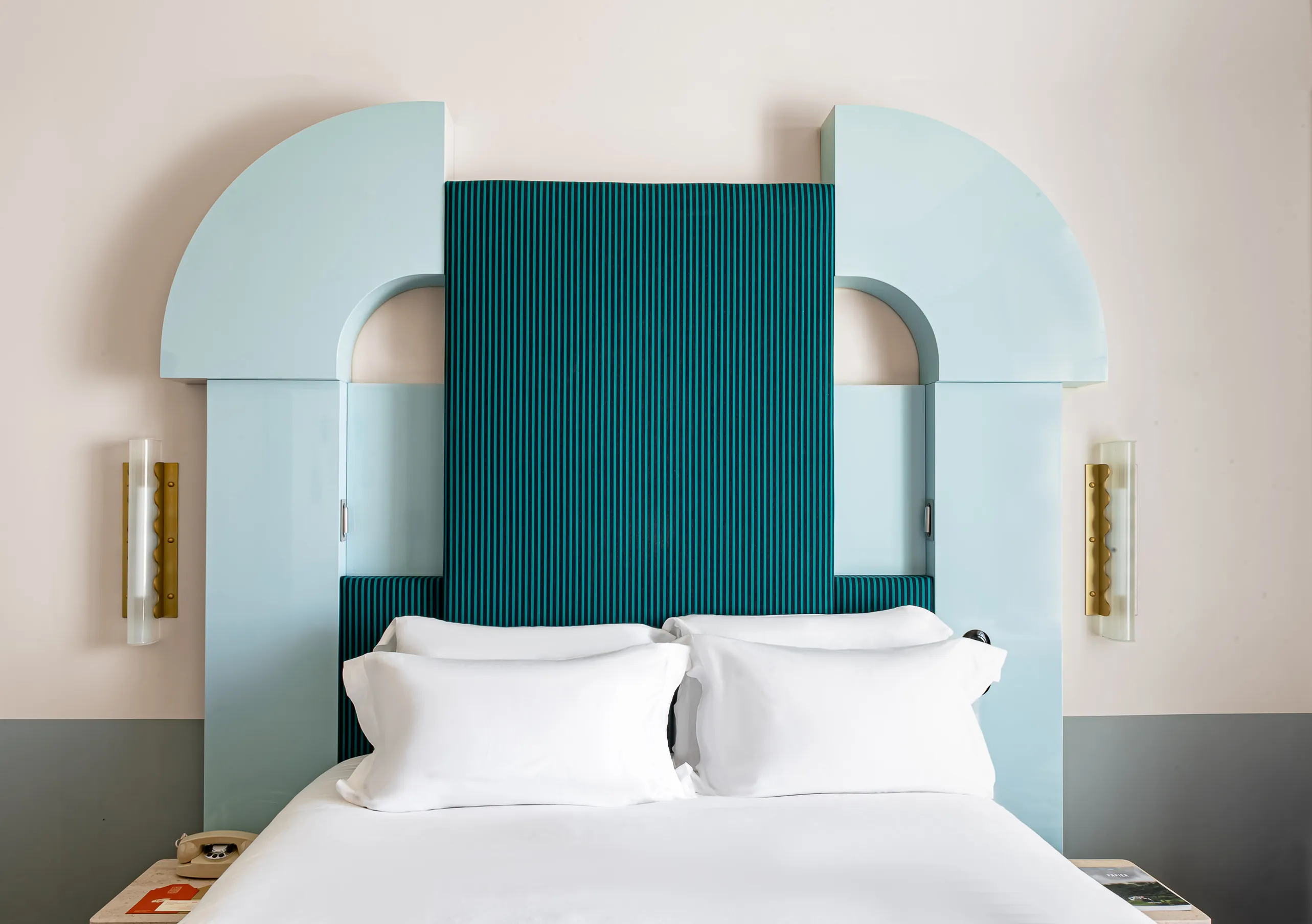 Experimental Group boutique hotel bedroom featuring emerald green channeled headboard with gold wall sconces and white linen bedding