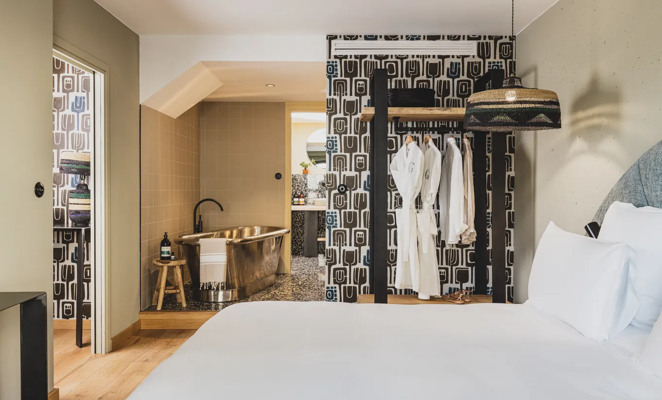 Experimental Group boutique hotel bedroom with open wardrobe, hanging robes and eclectic patterned wallpaper