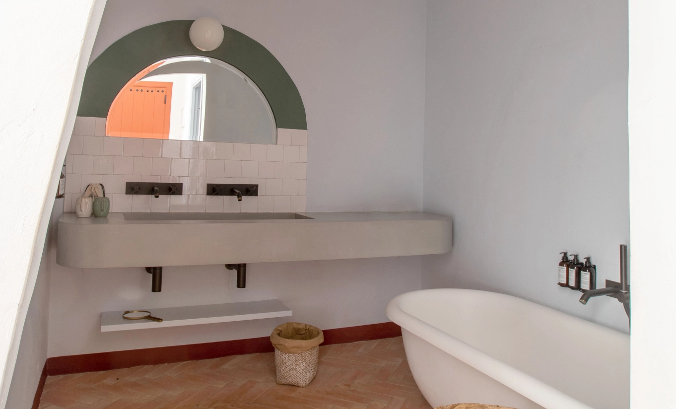 Menorca Experimental by Experimental Group – sculptural bathroom with arched alcove bathtub, concrete double vanity and skylight overhead