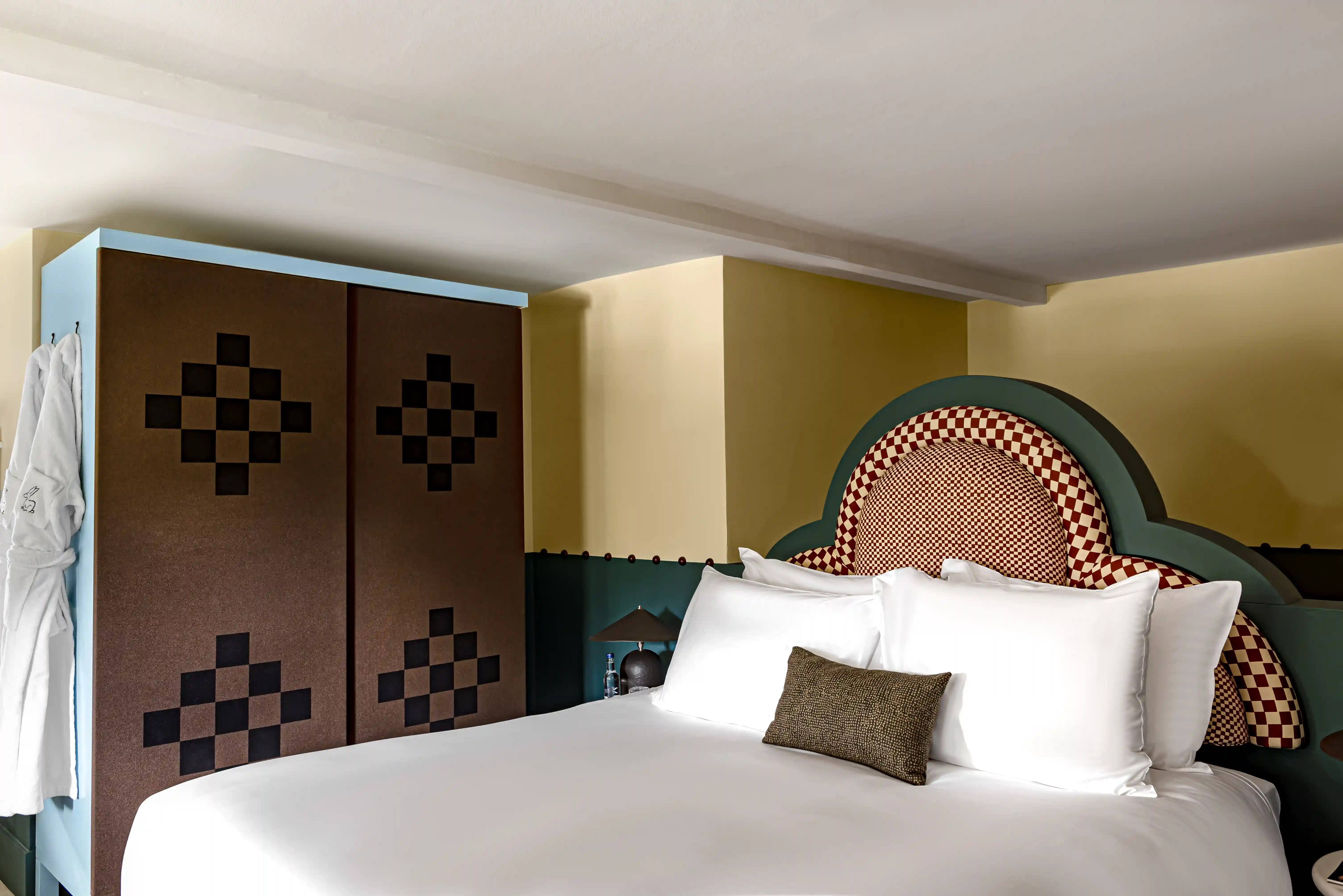 Bedroom with a four-poster bed, mustard yellow walls and lush indoor plants in the Wildflower room at Cowley Manor Experimental, Cotswolds