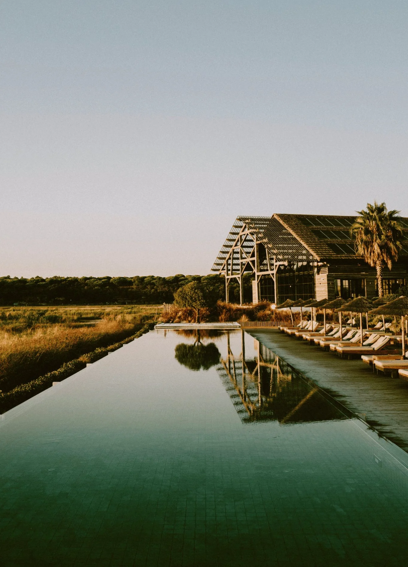 Exterior view of an elegant wooden structure by an infinity pool, capturing the serenity of the location at dusk.