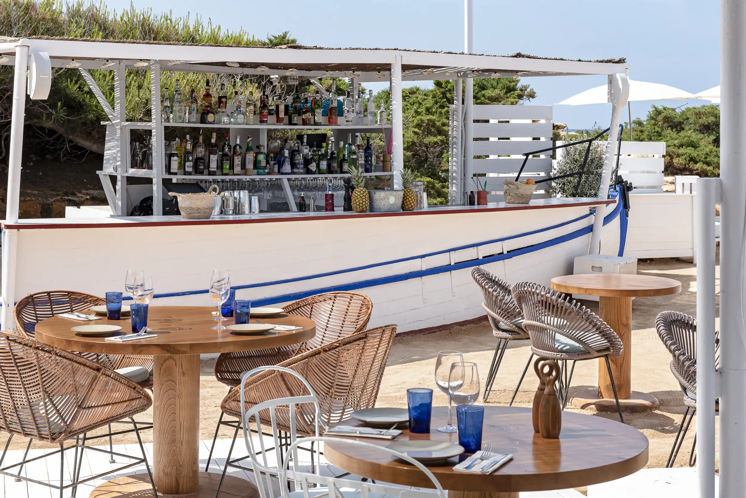 A welcoming outdoor terrace furnished with wooden tables, rattan chairs, and a bar designed to resemble a boat.