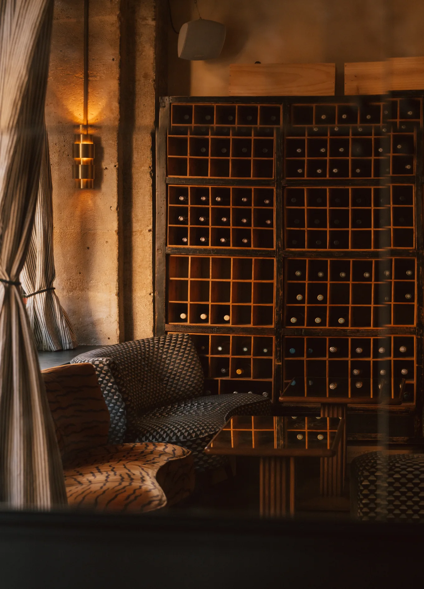 Aconchegante interior de La Compagnie St Germain, com iluminação suave, apresentando uma área de lounge confortável e uma grande garrafeira de madeira ao fundo.