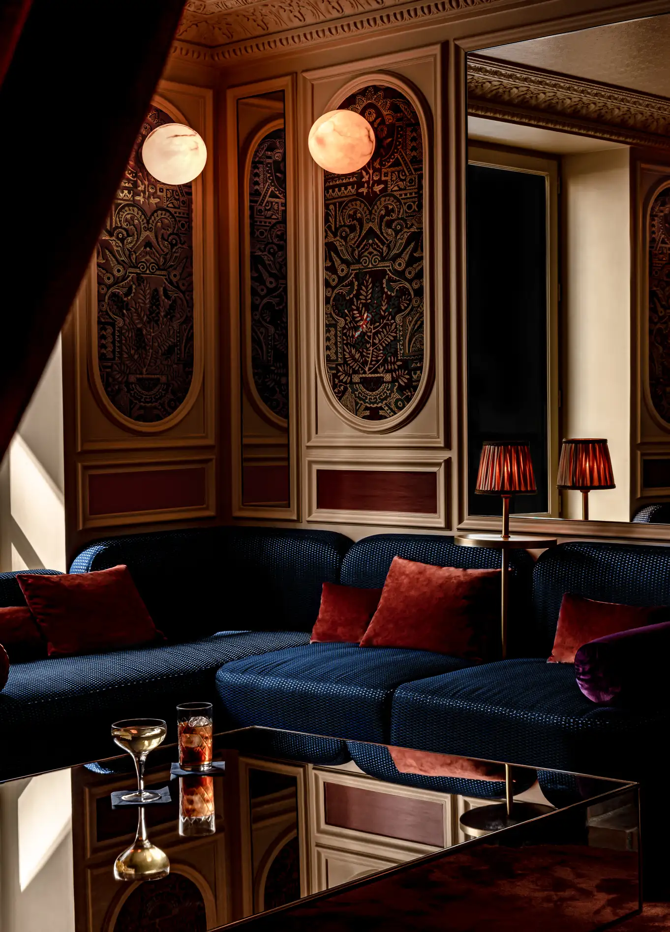 Uma área de lounge acolhedora com sofás azul-escuro, almofadas vermelhas e iluminação suave, criando uma atmosfera sofisticada.