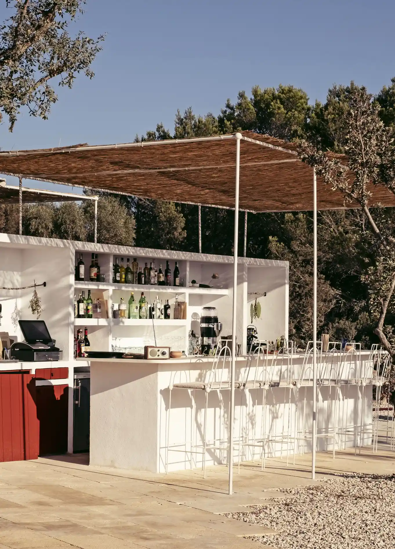 Bar de praia moderno e elegante ao ar livre, com uma estrutura branca e limpa sob uma pérgula de madeira, oferecendo um ambiente descontraído.