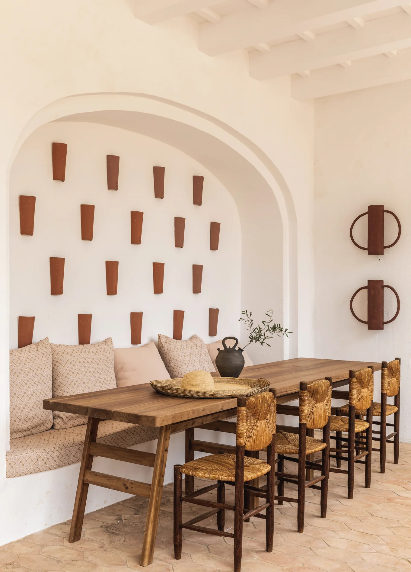 Visão geral do espaço de refeições no Menorca Experimental, combinando design rústico, banquetas confortáveis e decorações de parede artesanais sob um arco.