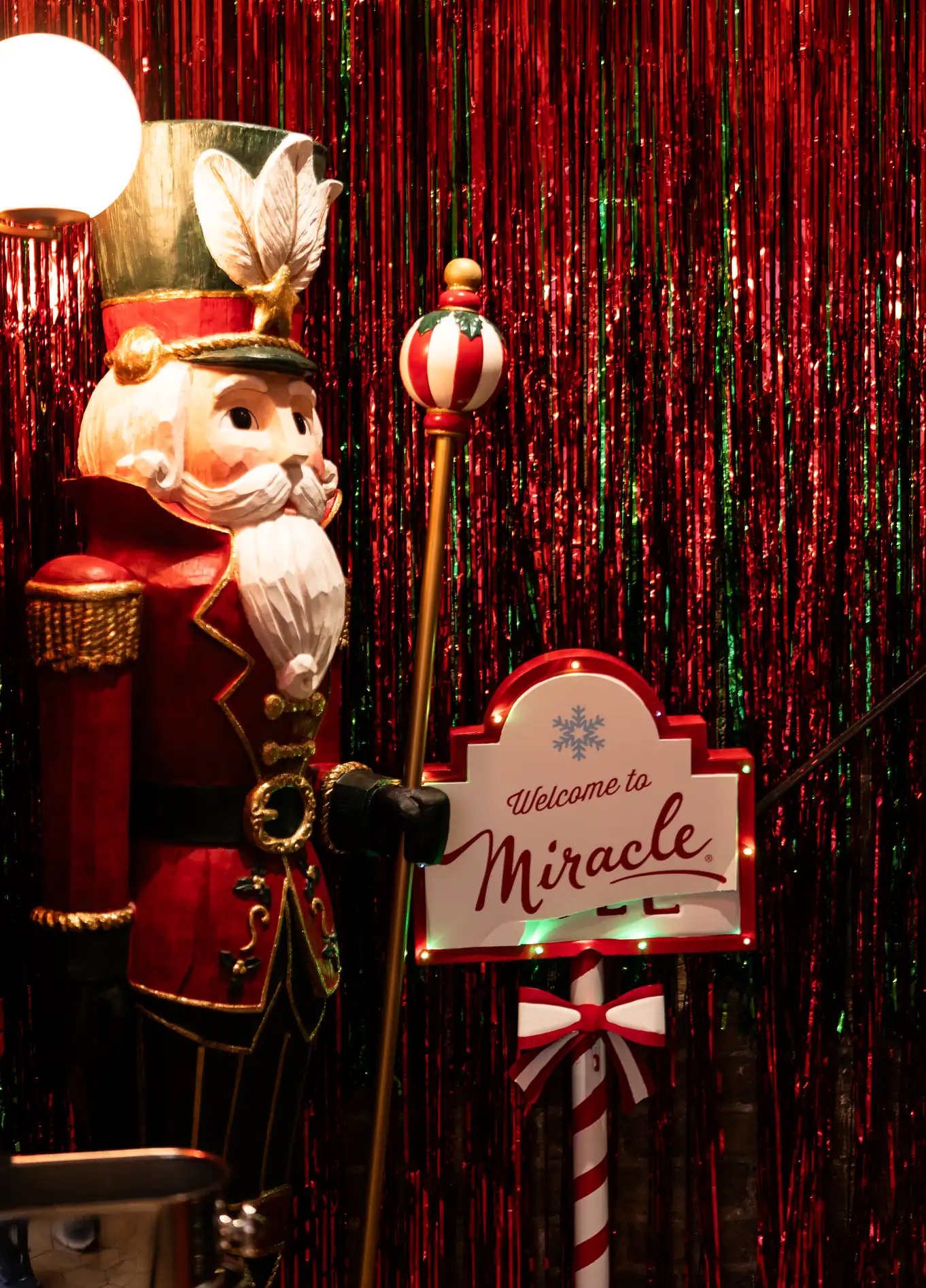 Wooden nutcracker soldier decoration holding a staff next to a lit sign saying 'Welcome to Miracle'.