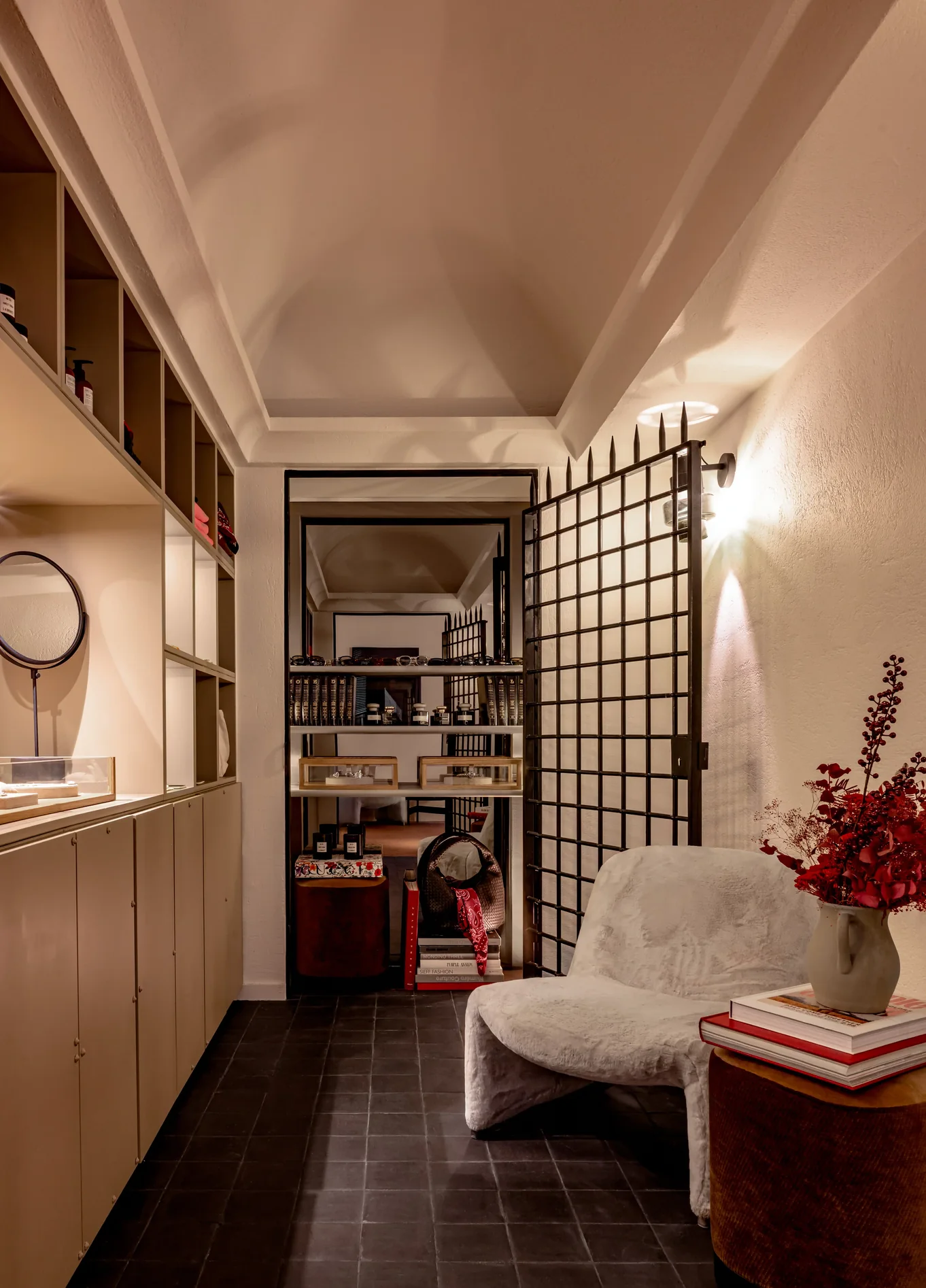 Boutique com iluminação acolhedora, estantes de madeira, poltrona aconchegante e ramo de flores vermelhas no Experimental Marais, hotel boutique de luxo no Marais, Paris.