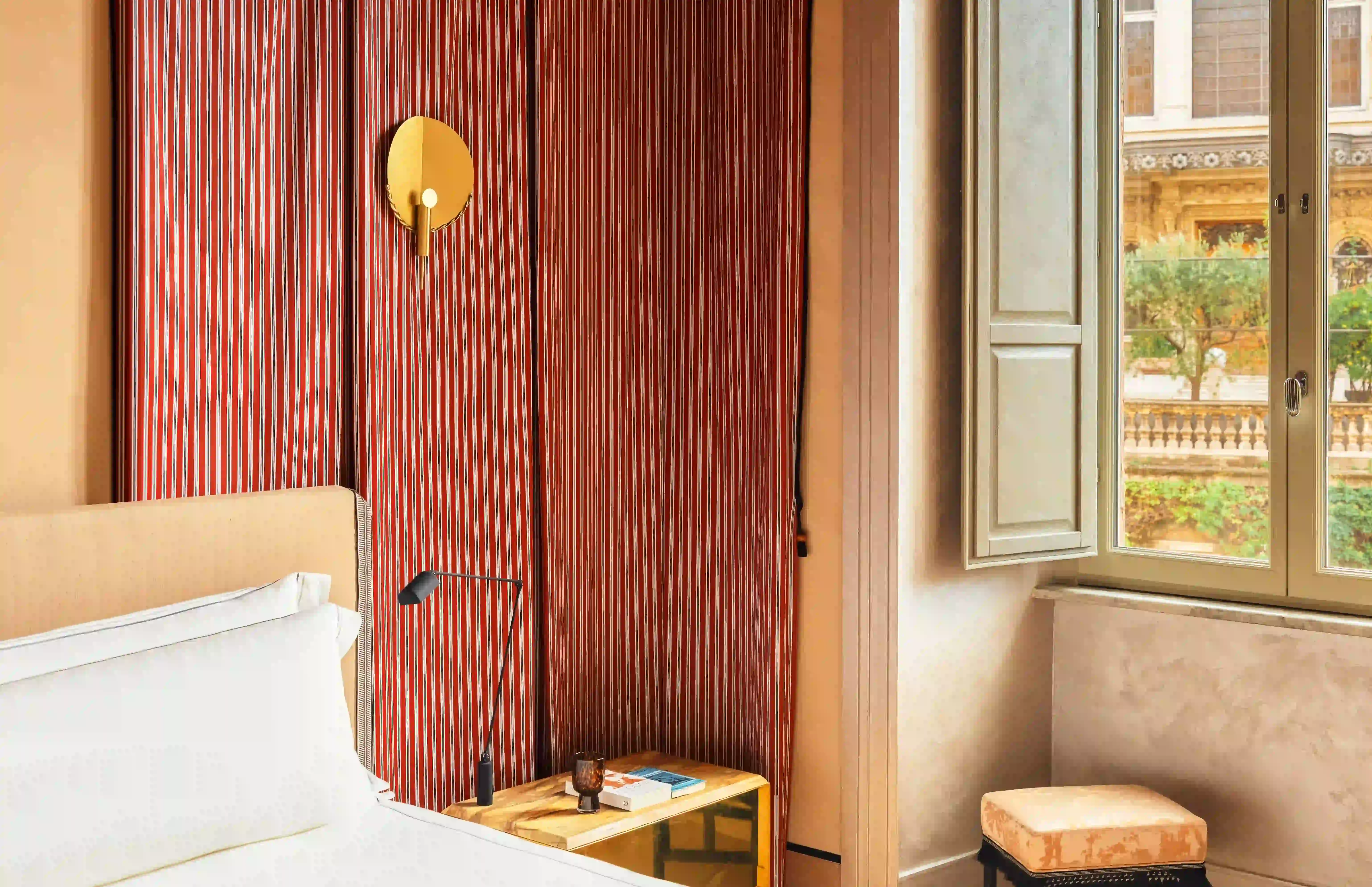 Chambre d'hôtel élégante avec lit, rideaux roses et vue sur la ville depuis la fenêtre.