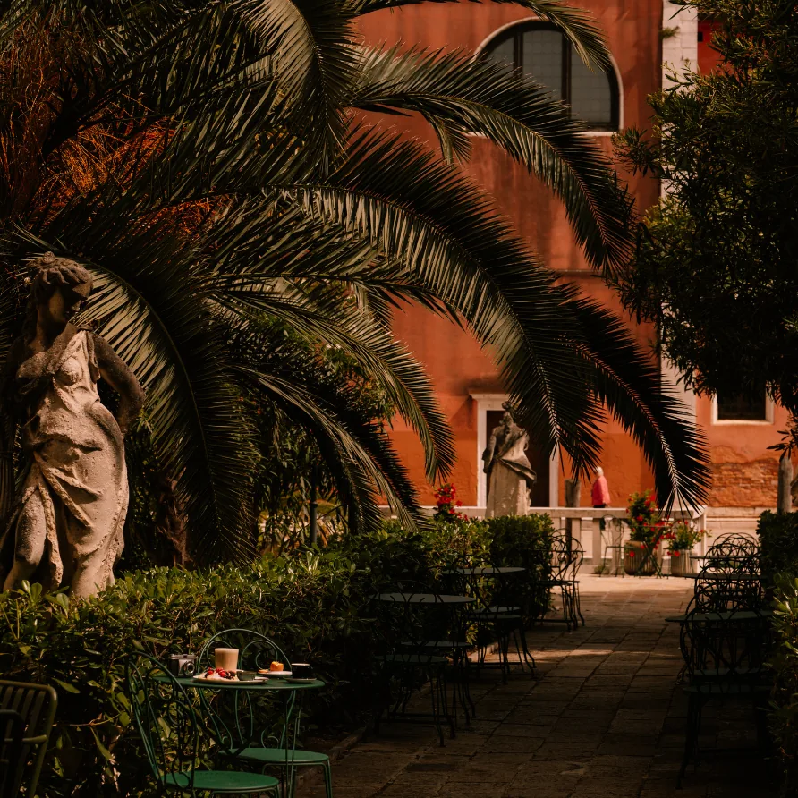 Venetian garden with palm tree, statues and green tables at Il Palazzo Experimental boutique hotel, Venice