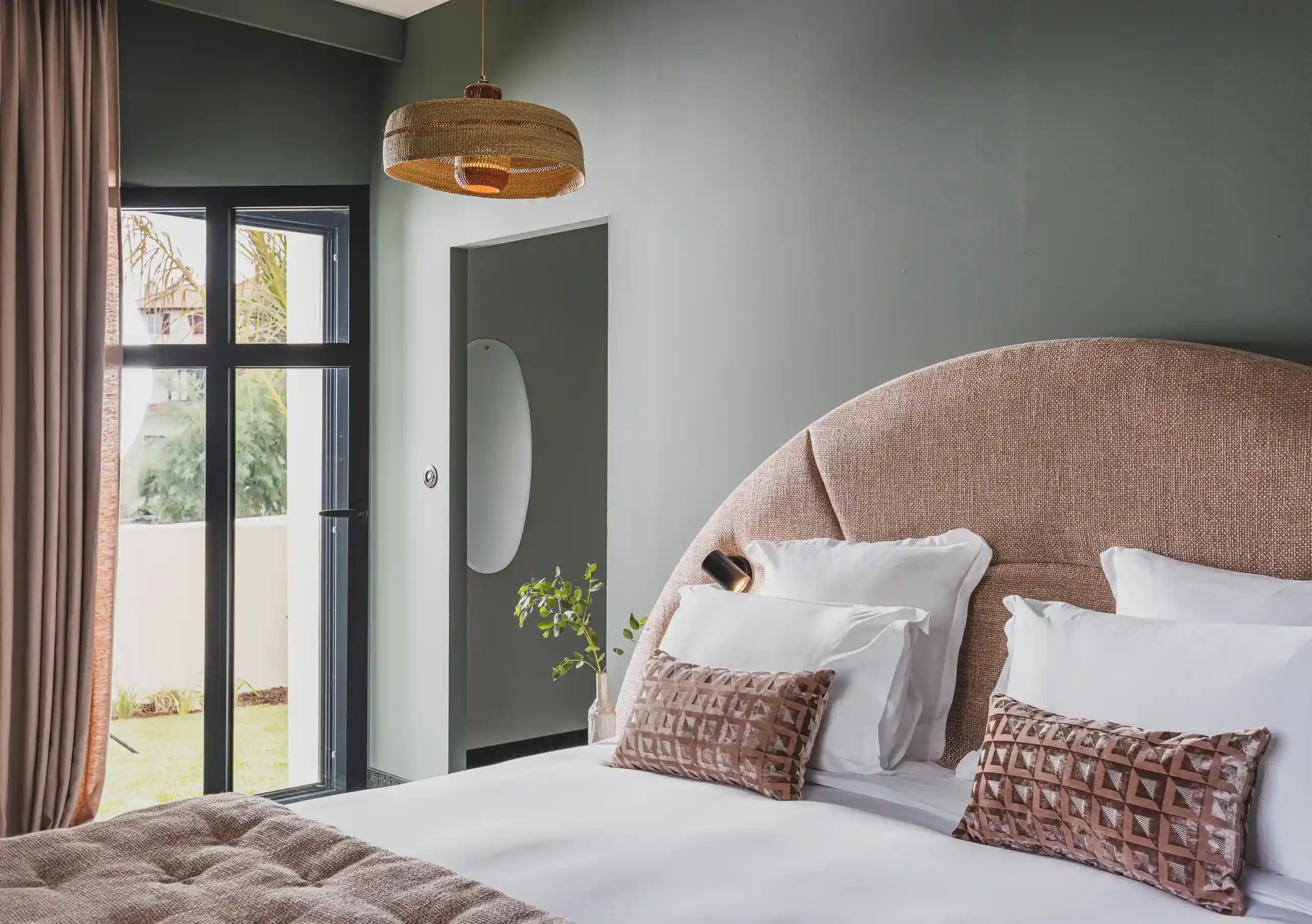 Experimental Group hotel bedroom with oversized blush pink rounded headboard, white bedding, pink cushions, and soft grey walls.