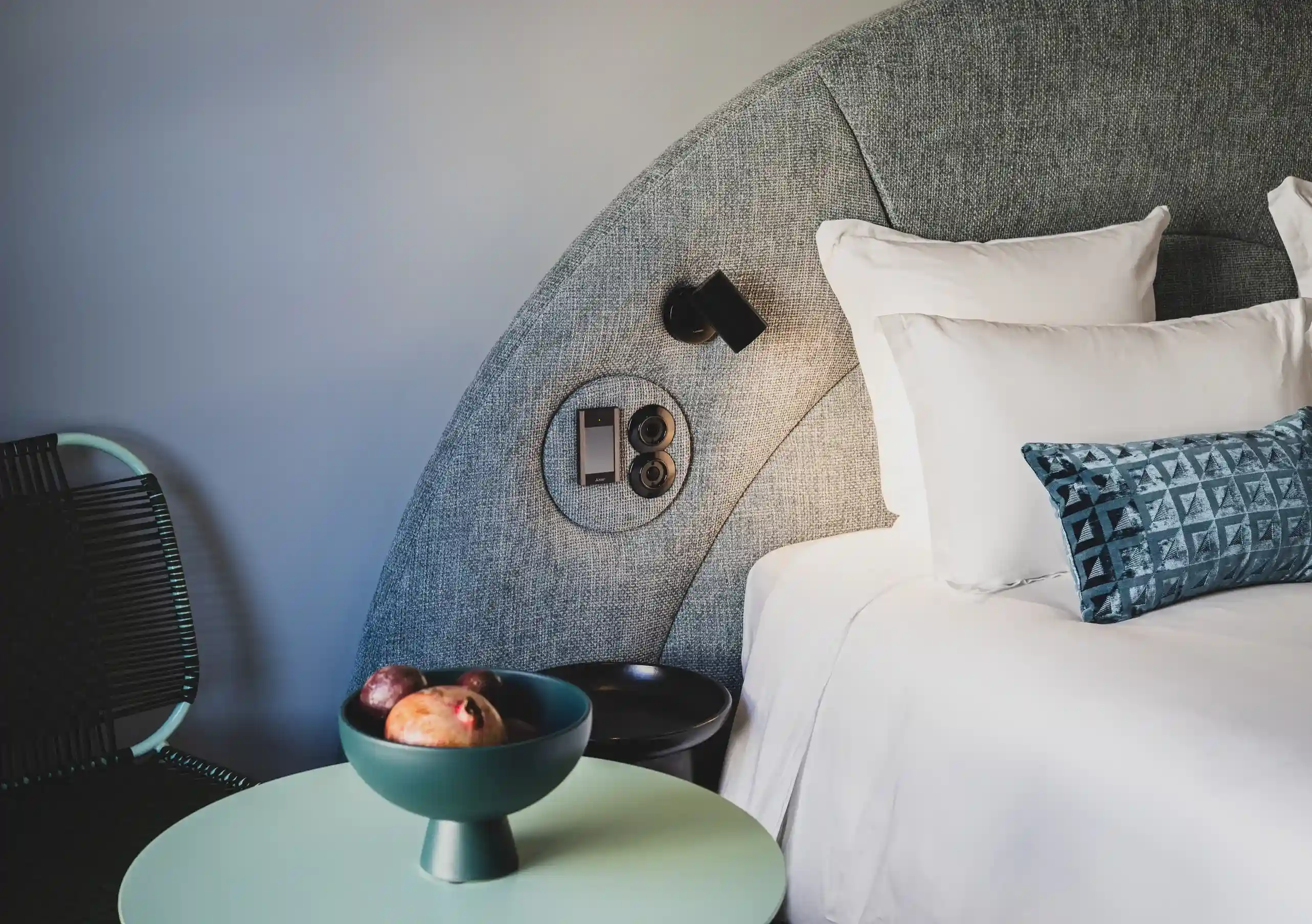Le Garage Biarritz Experimental hotel bedroom with curved grey headboard, white bedding, blue accent cushions, and warm ambient lighting.